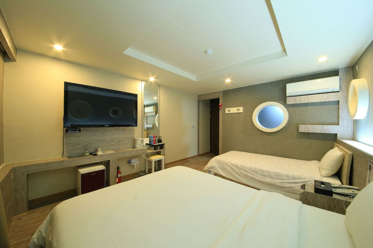 A hotel room with two beds, a TV, a mirror, a small desk, and a bathroom with a toilet and sink.