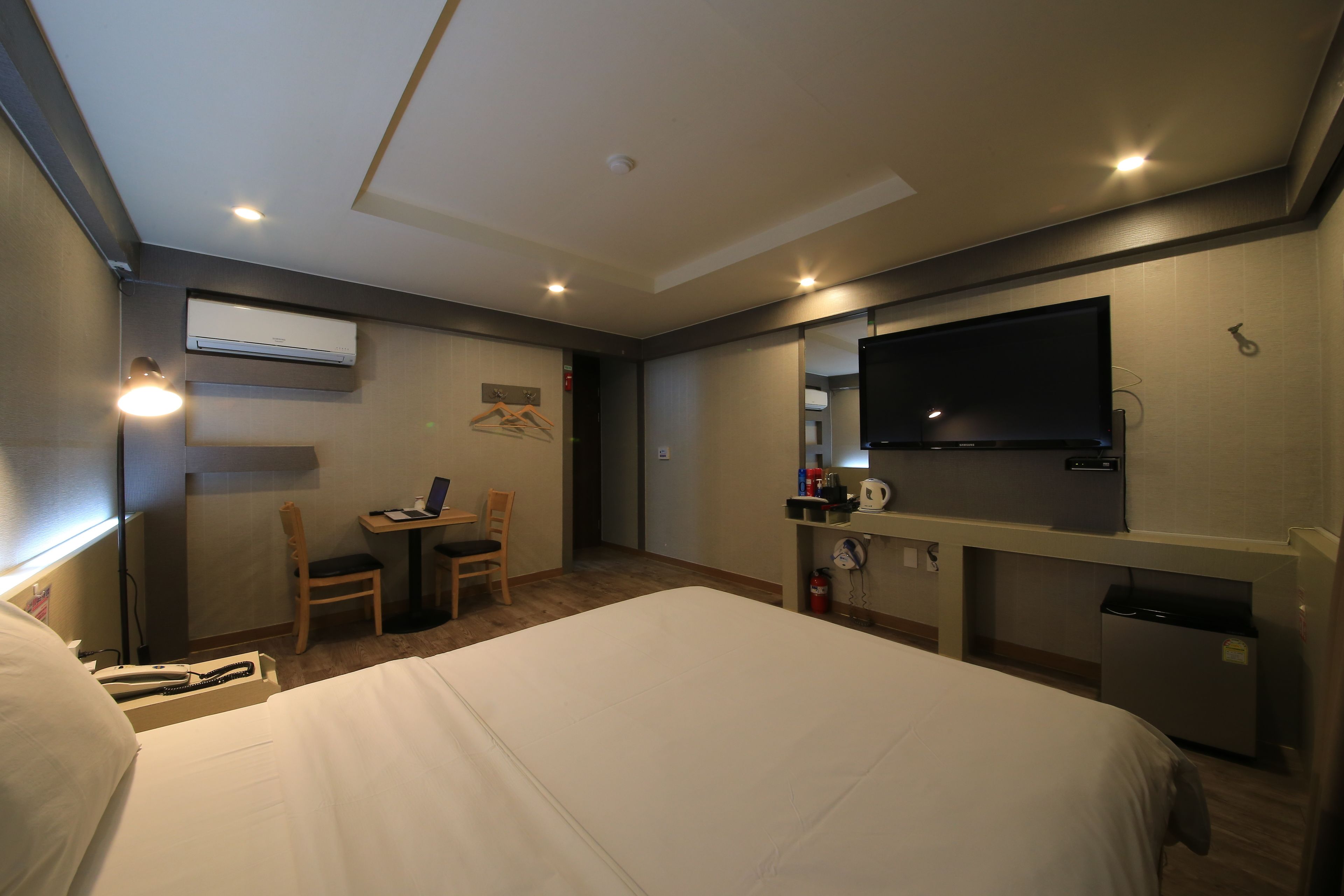 A hotel room with a large bed, a desk with a chair, a television, and an air conditioning unit.