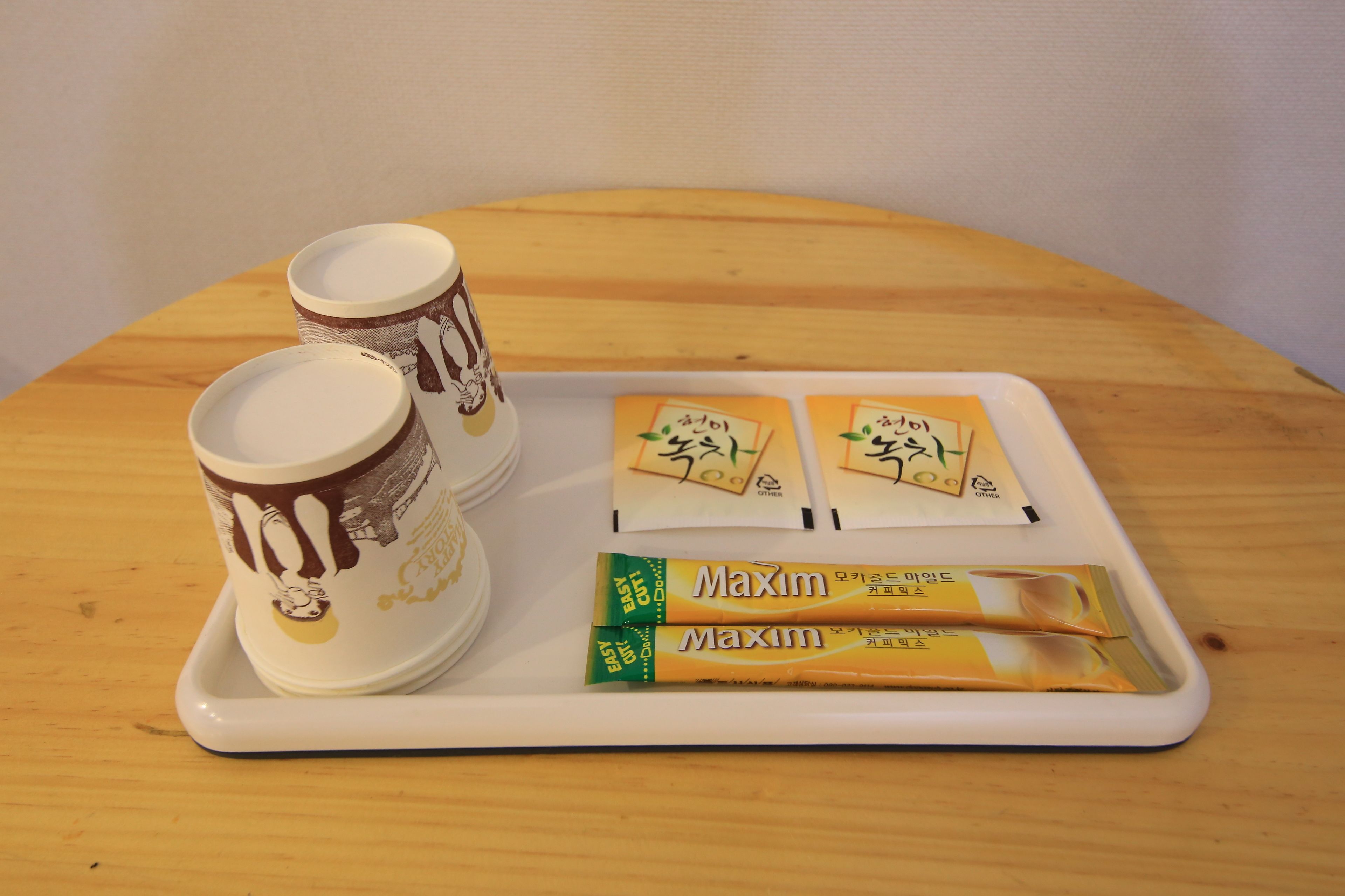 En bakke med to kaffekopper og to pakker Maxim te på et træbord.
