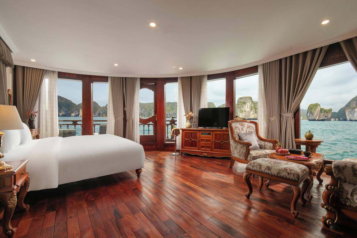 Amplia habitación con una cama grande, suelo de madera, televisión y vista al mar.