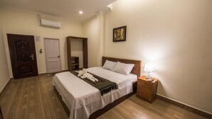 Una habitación de hotel con una cama grande, una mesita de noche de madera, aire acondicionado instalado en la pared y una puerta.