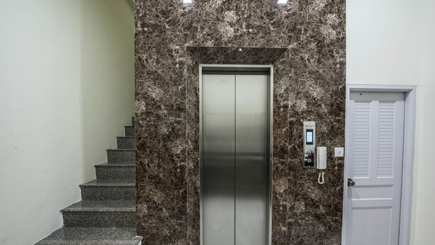 Una escalera de mármol conduce a un ascensor con una puerta blanca a un lado.