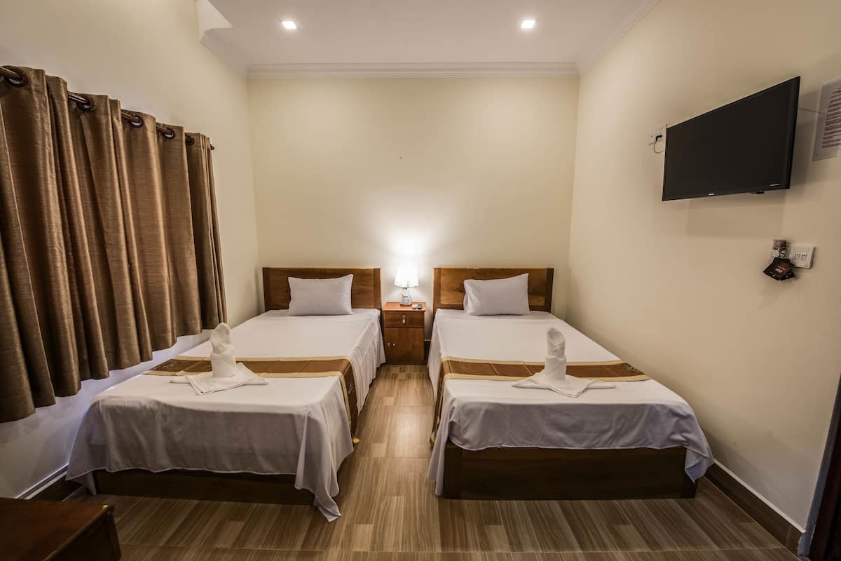 Quarto de hotel com duas camas de solteiro, televisão fixada na parede e piso de madeira.