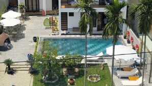 A multi-story hotel with a swimming pool, outdoor seating, and palm trees.