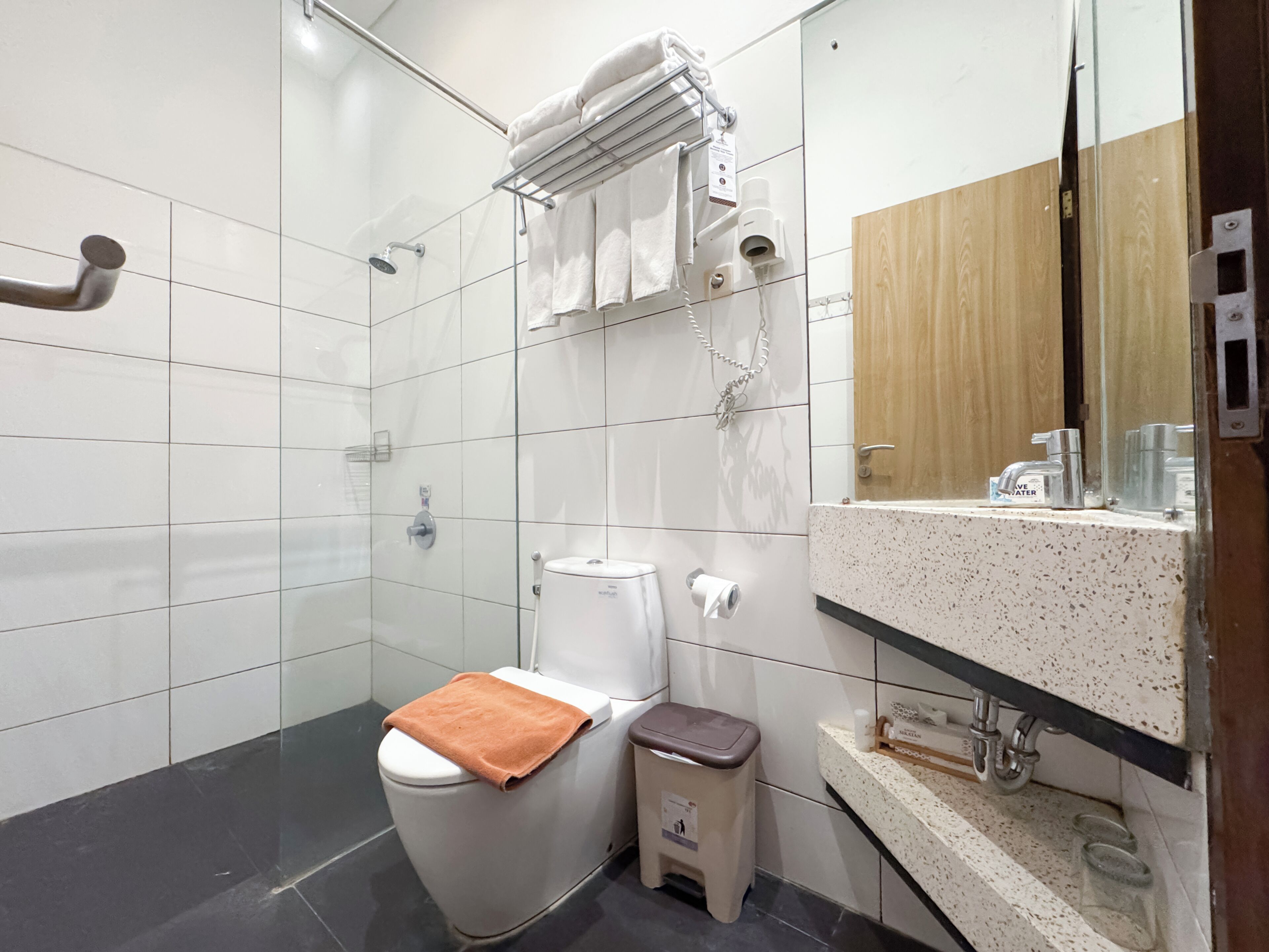 Un baño moderno con cabina de ducha de vidrio, inodoro con toalla, un cubo de basura y lavamanos con espejo.