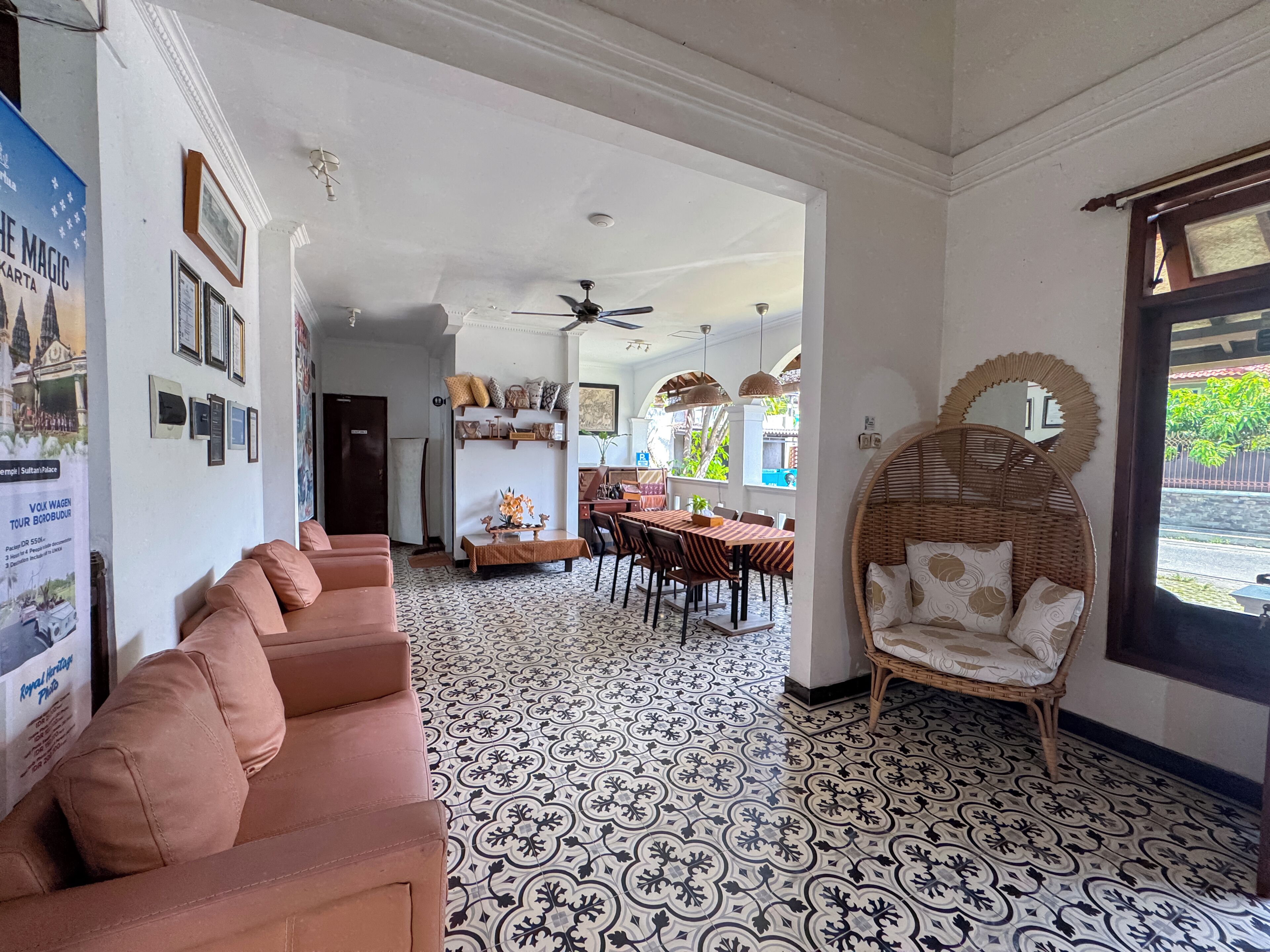 A room with a patterned floor, a sofa, a wicker chair, a dining area with chairs and a table, and a ceiling fan.