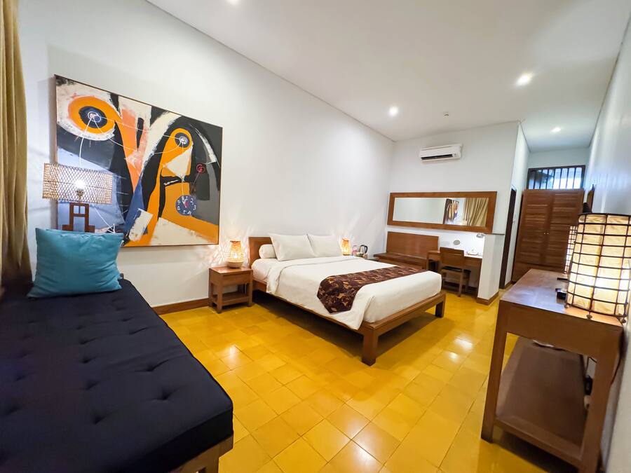 Una camera d'hotel con un letto, comodino, lampada, opere d'arte, scrivania, sedia e armadio.