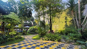 Un sentier de jardin au motif à carreaux, bordé d’une végétation luxuriante et d’arbres.
