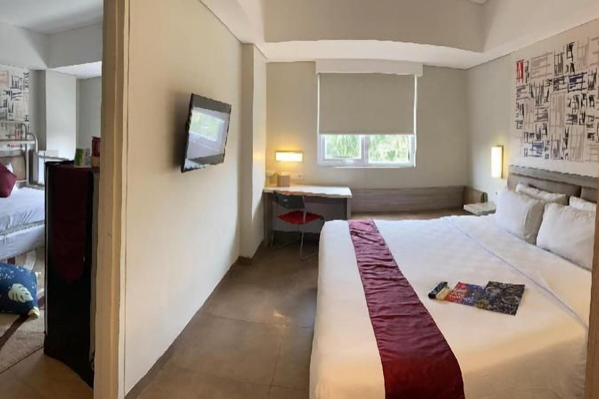 Una habitación de hotel con cama, escritorio, silla, televisor y ventana.