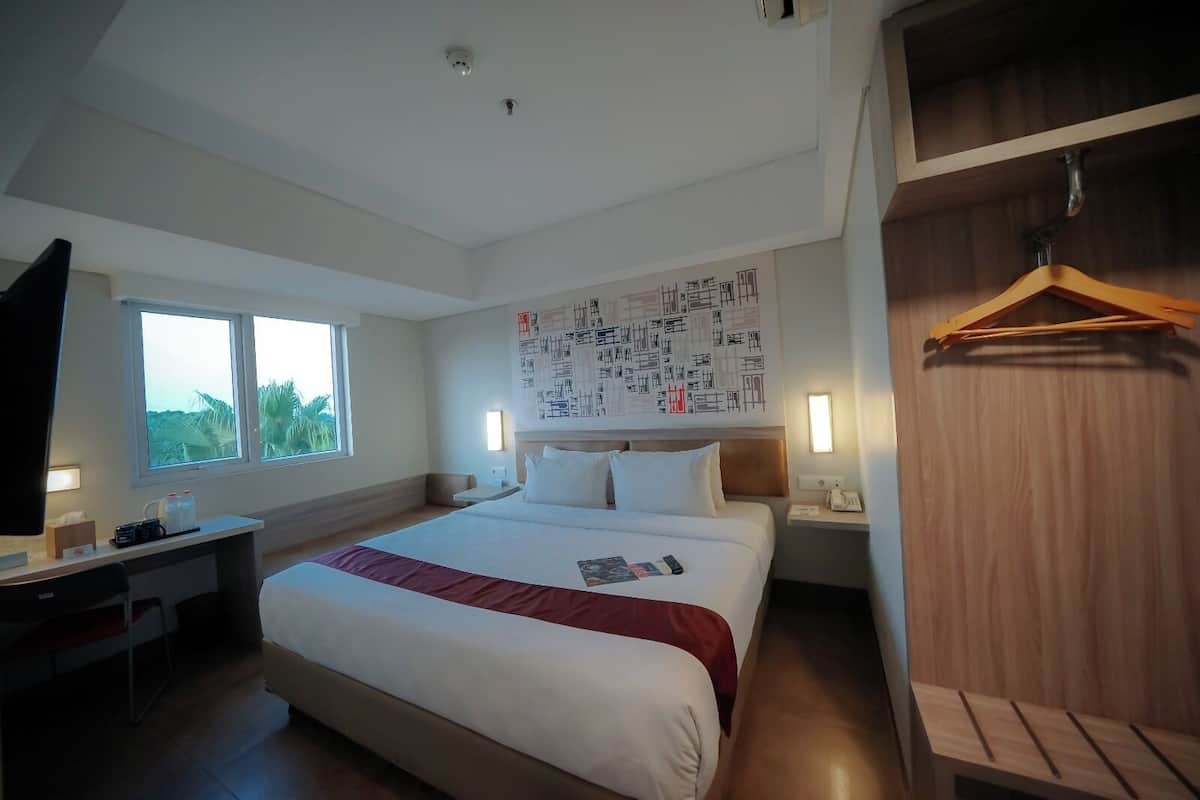Habitación de hotel con una cama grande, mesitas de noche, un escritorio con silla, un armario y un ventanal amplio.