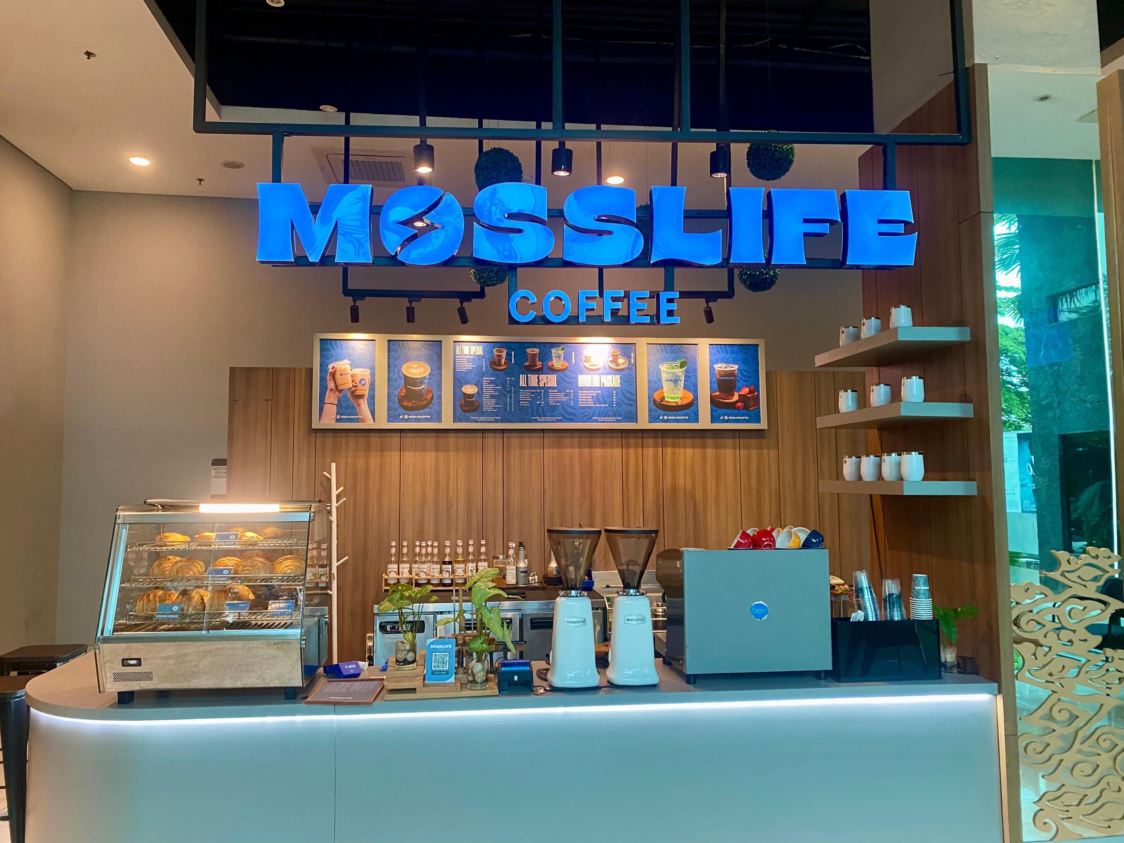 Ein Café namens Moss Life mit modernem Interieur, einer Kaffeemaschine und einer Speisekarte über der Theke.