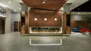 A modern lobby with a wooden reception desk, pendant lights, and a large aquarium. - Grand Cordela Hotel Bandung (Bandung)