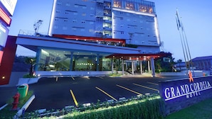 A modern hotel with a glass facade, a covered entrance, and a parking lot. - Grand Cordela Hotel Bandung (Bandung)
