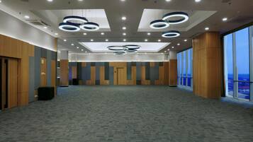 A spacious conference room with a high ceiling, circular light fixtures, and large windows offering a view.