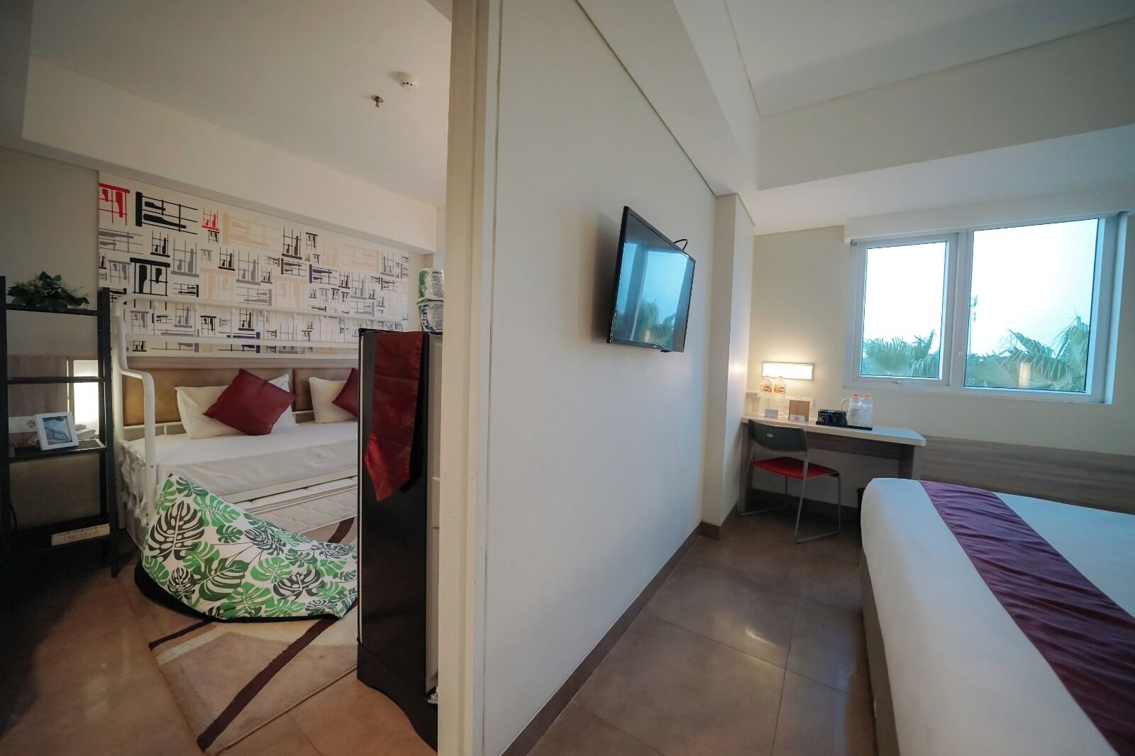 A hotel room with a bunk bed, a desk with a chair, a TV mounted on the wall, and a window with a view.