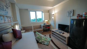 A compact hotel room with a bed, a desk, a television, and a refrigerator.