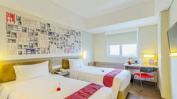 Habitación de hotel con dos camas, un escritorio, una silla, una ventana y una pared decorada con arte abstracto.