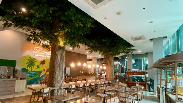 A restaurant with indoor trees, wooden tables, and chairs. - Grand Cordela Hotel Bandung (Bandung)