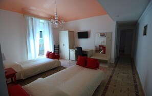A hotel room with two beds, a desk, a TV, and a view of the outside.
