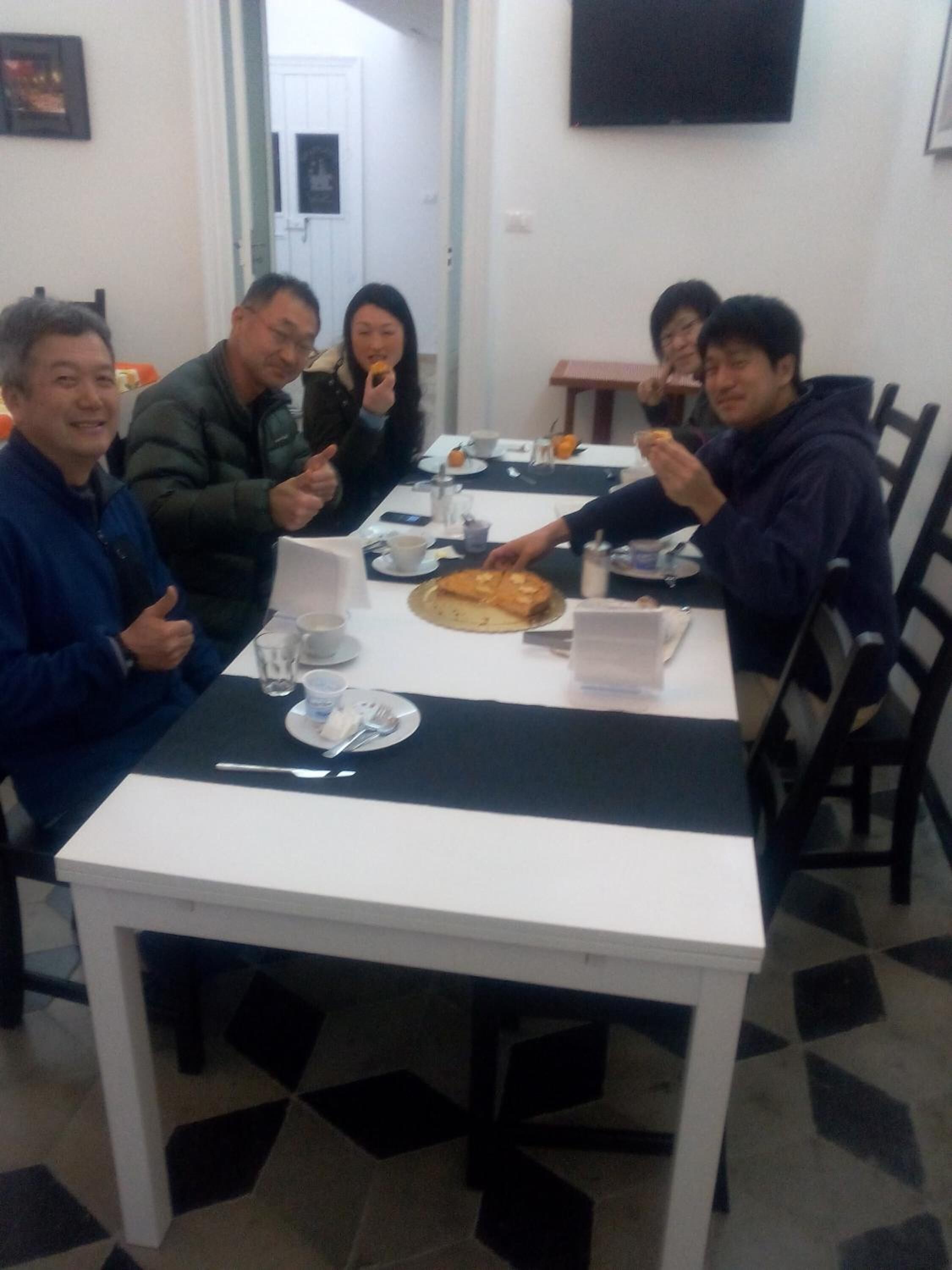 A group of people dining at a table with a white tablecloth, plates, cups, and a pizza.