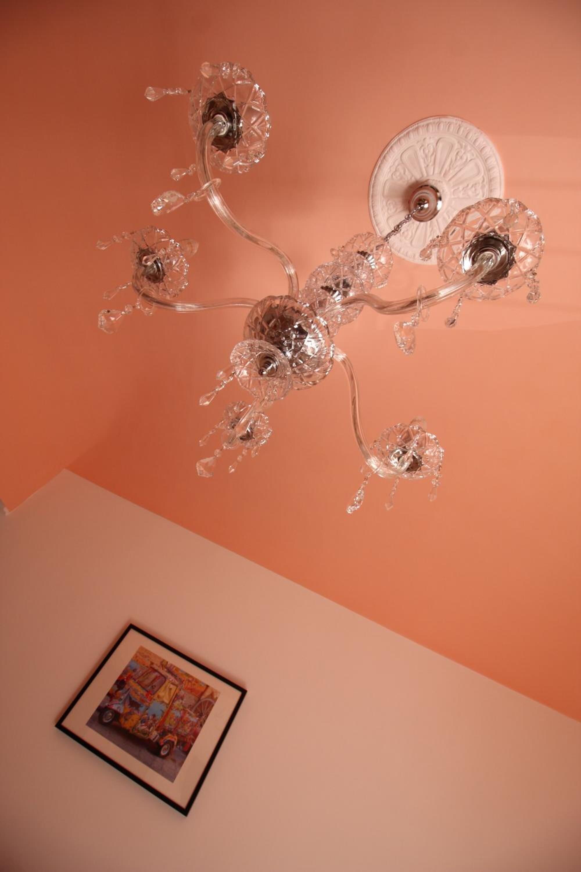 Un lustre doté de plusieurs bras en cristal et d’une rosace blanche au plafond.