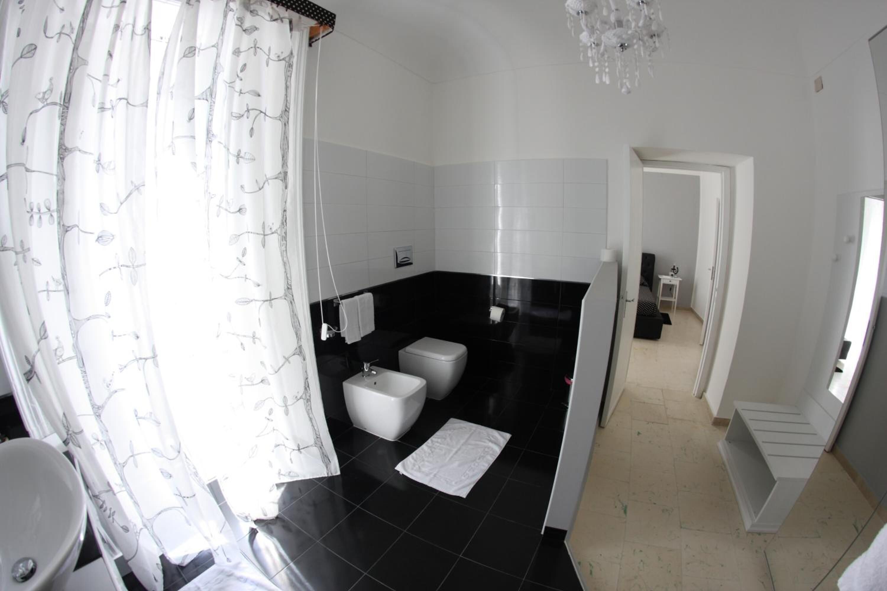A modern bathroom with a black and white tiled floor, a white sink, a bidet, and a shower curtain with a tree pattern.