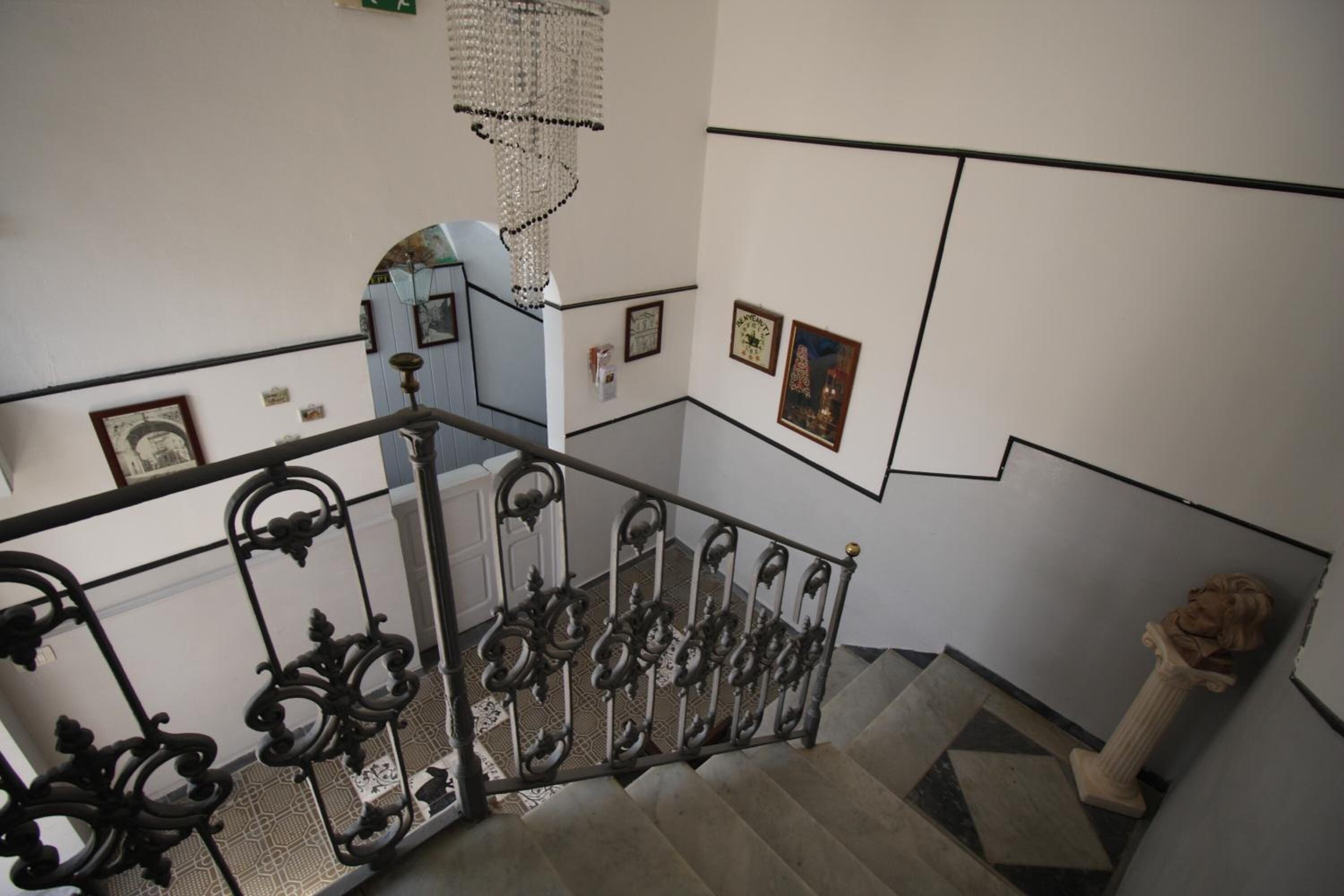 Una escalera con barandillas de metal negro ornamentadas, un candelabro y una columna con una estatua.