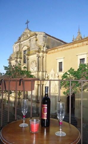 A table with a bottle of wine and two glasses, set against a backdrop of a historic building with ornate architecture.