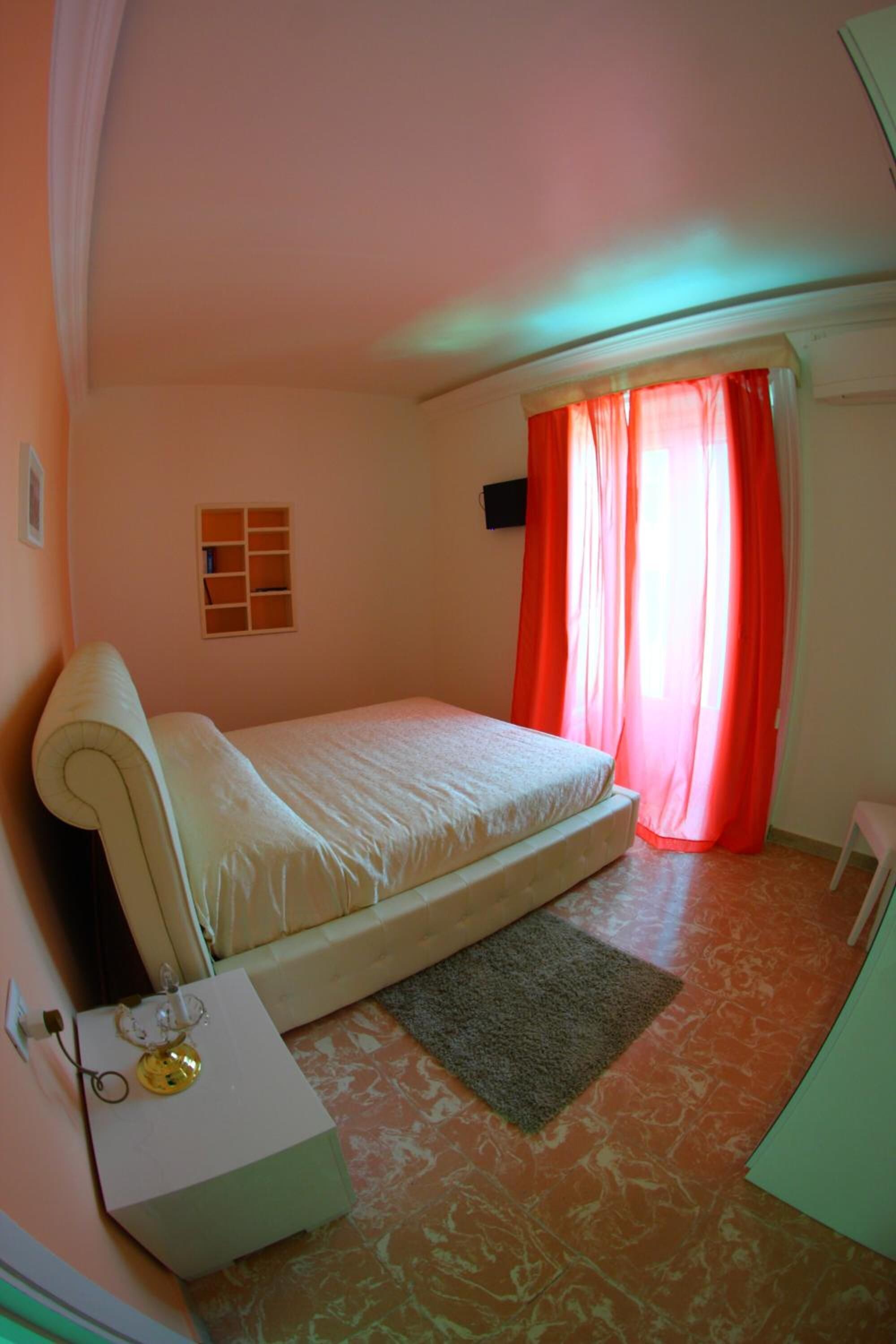 Une chambre à coucher avec un lit simple, une table de chevet, une petite armoire et une fenêtre avec des rideaux rouges.