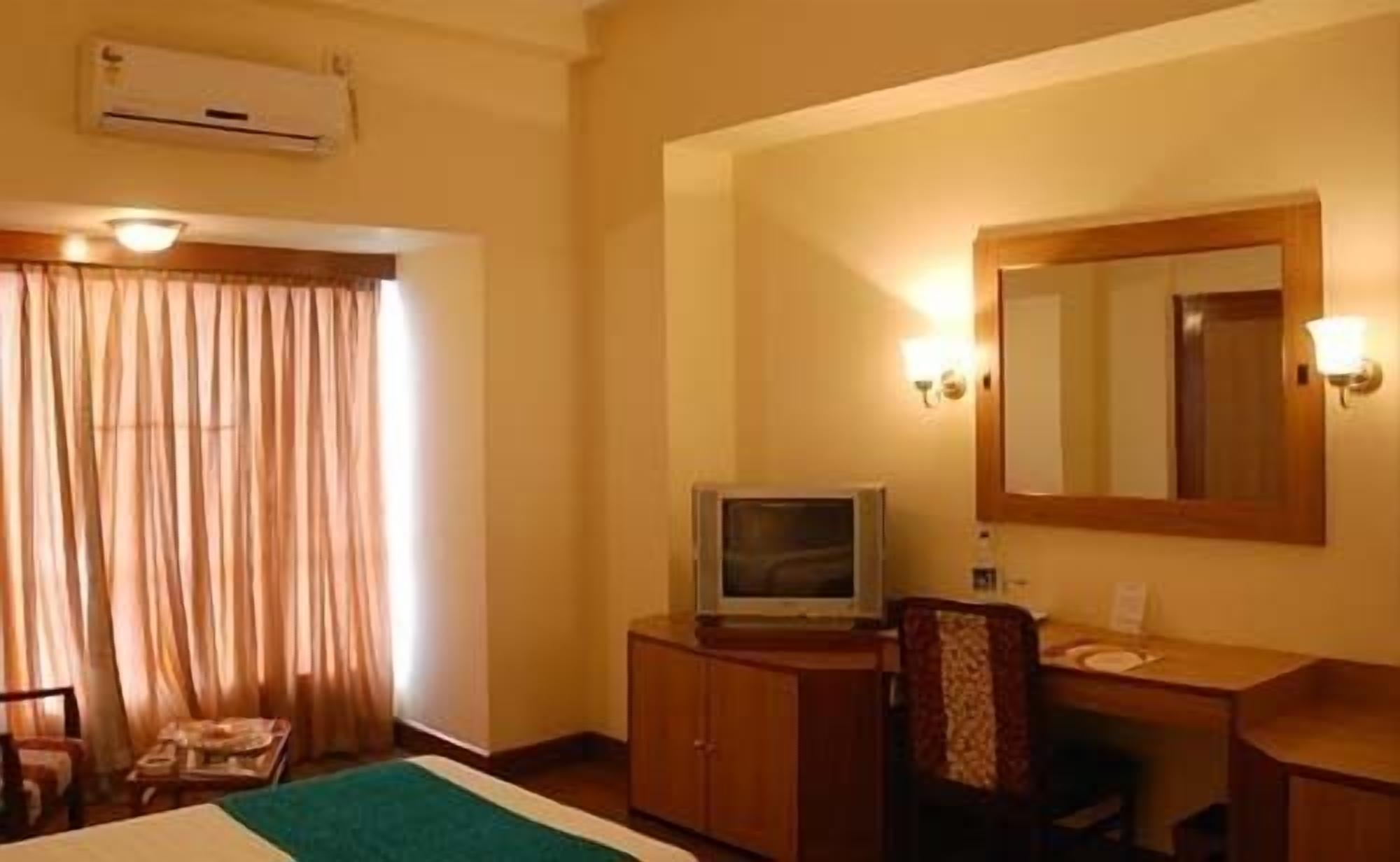 A hotel room with a bed, a desk with a television, a chair, and a window with curtains.