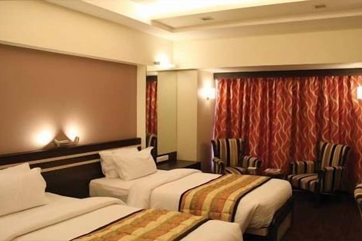 A hotel room with two beds, a seating area with striped chairs, and a large window with red curtains.
