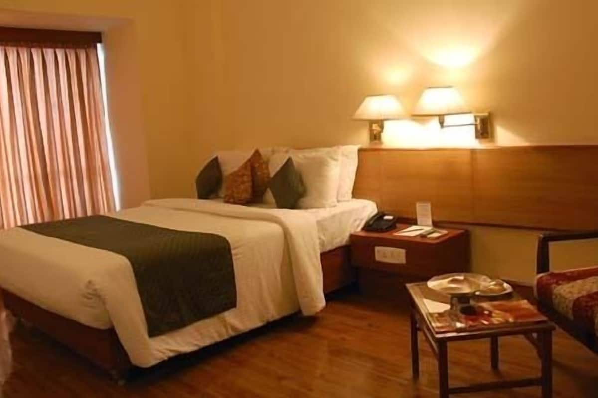 A hotel room with a bed, bedside table, lamp, chair, and a wooden floor.
