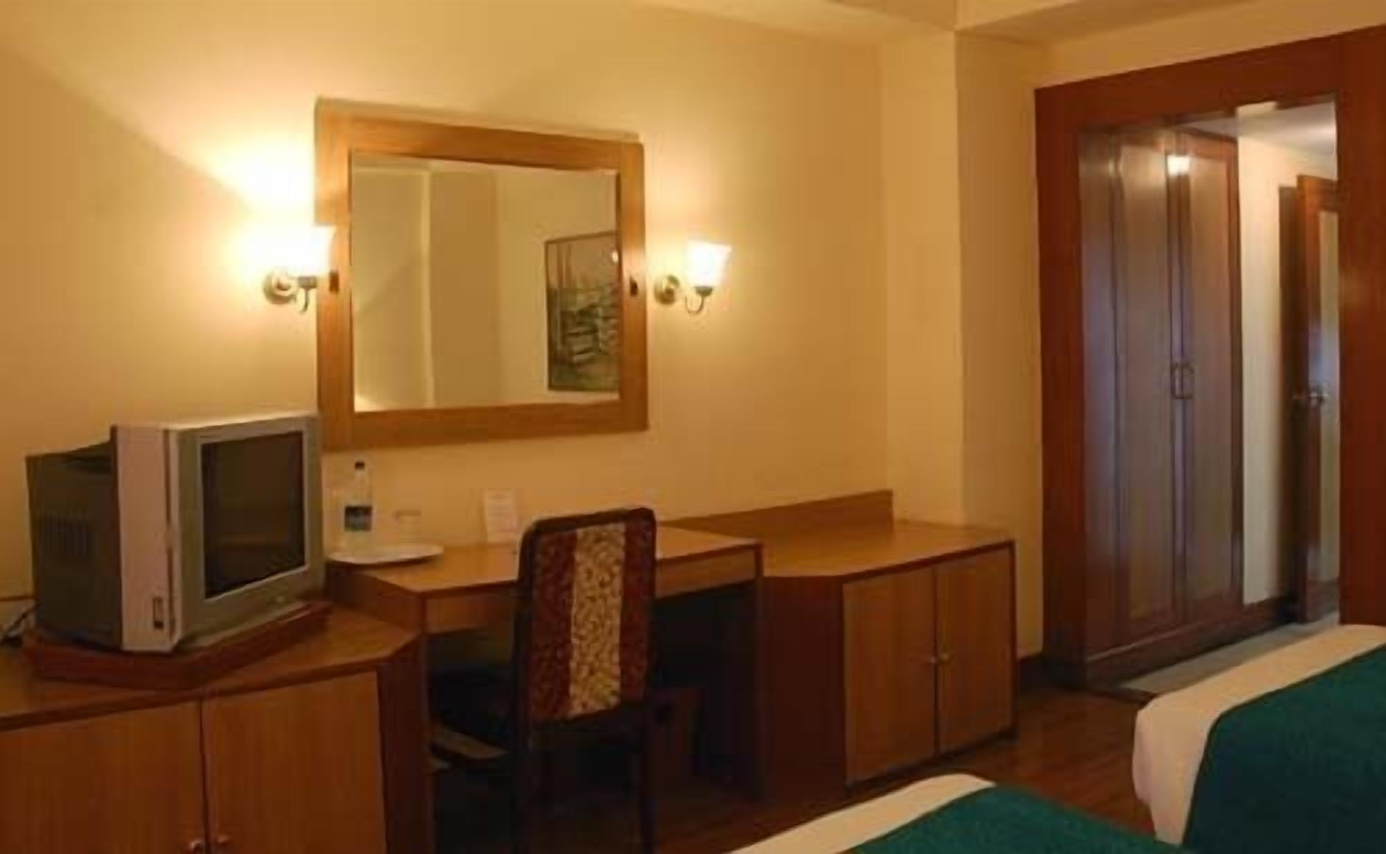 A hotel room with a desk, a chair, a bed, a television, and a wardrobe.