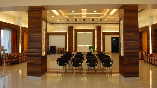 Una amplia sala de conferencias con filas de sillas orientadas hacia una pantalla grande, paneles de madera y suelo pulido.
