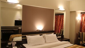 Habitación de hotel con una cama grande, una mesita de noche con teléfono, un espejo y un televisor montado en la pared.