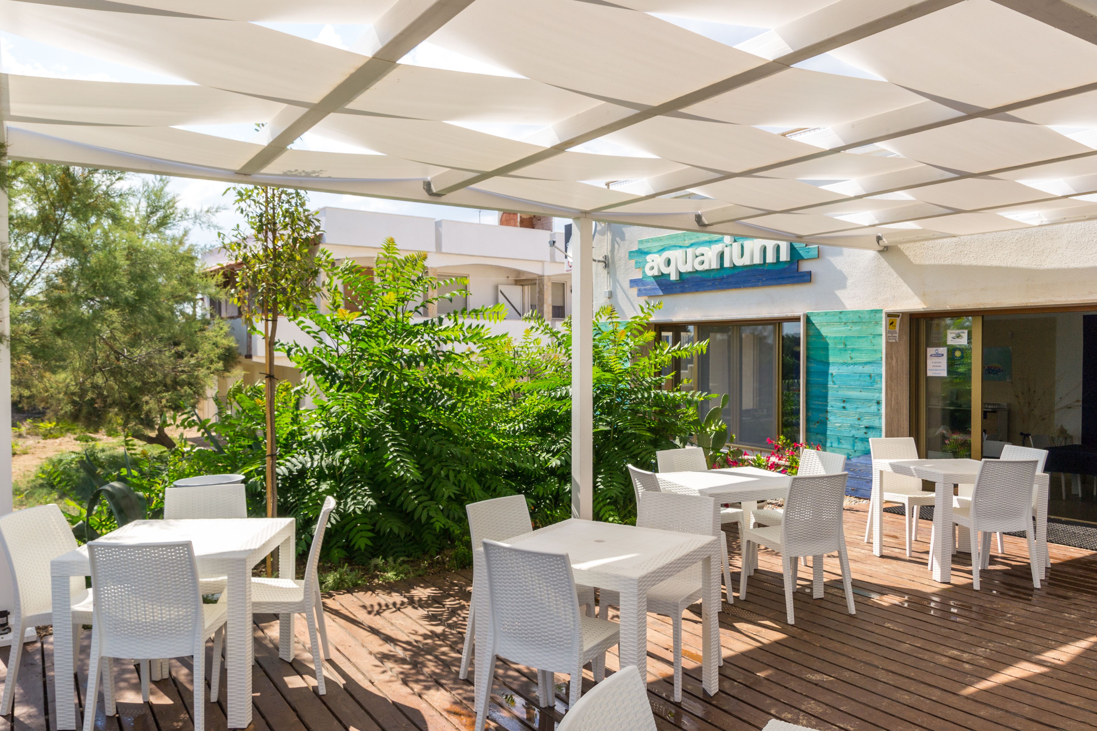 Un área de patio al aire libre con mobiliario de mimbre blanco y un cartel que dice 'aquarium'.