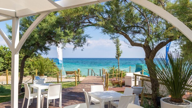An outdoor patio with white wicker furniture, a wooden deck, and a view of the sea. - Aquarium Residence (Manduria)