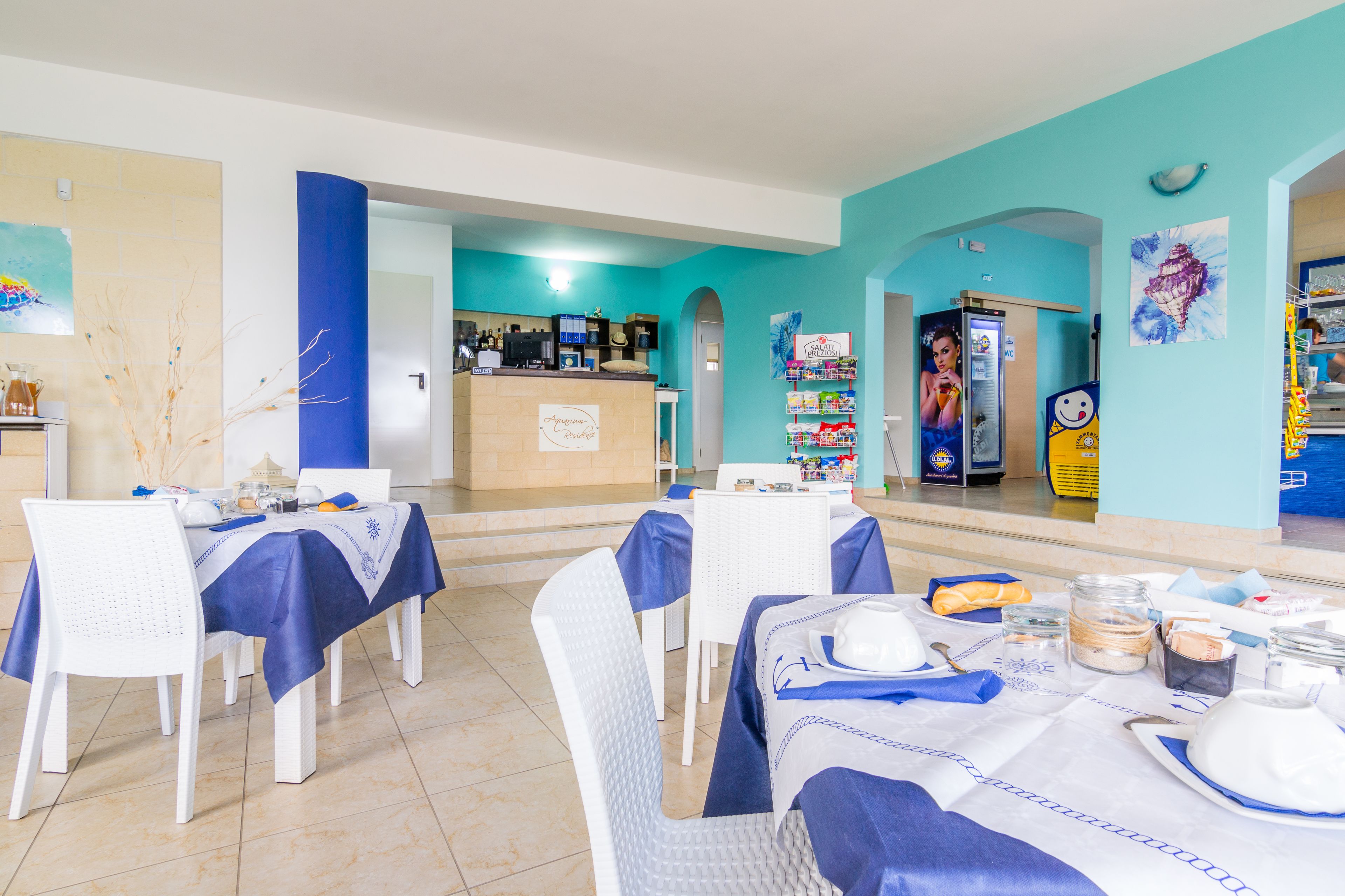 A restaurant with blue and white decor, tables set with white chairs, and a counter area with a menu.