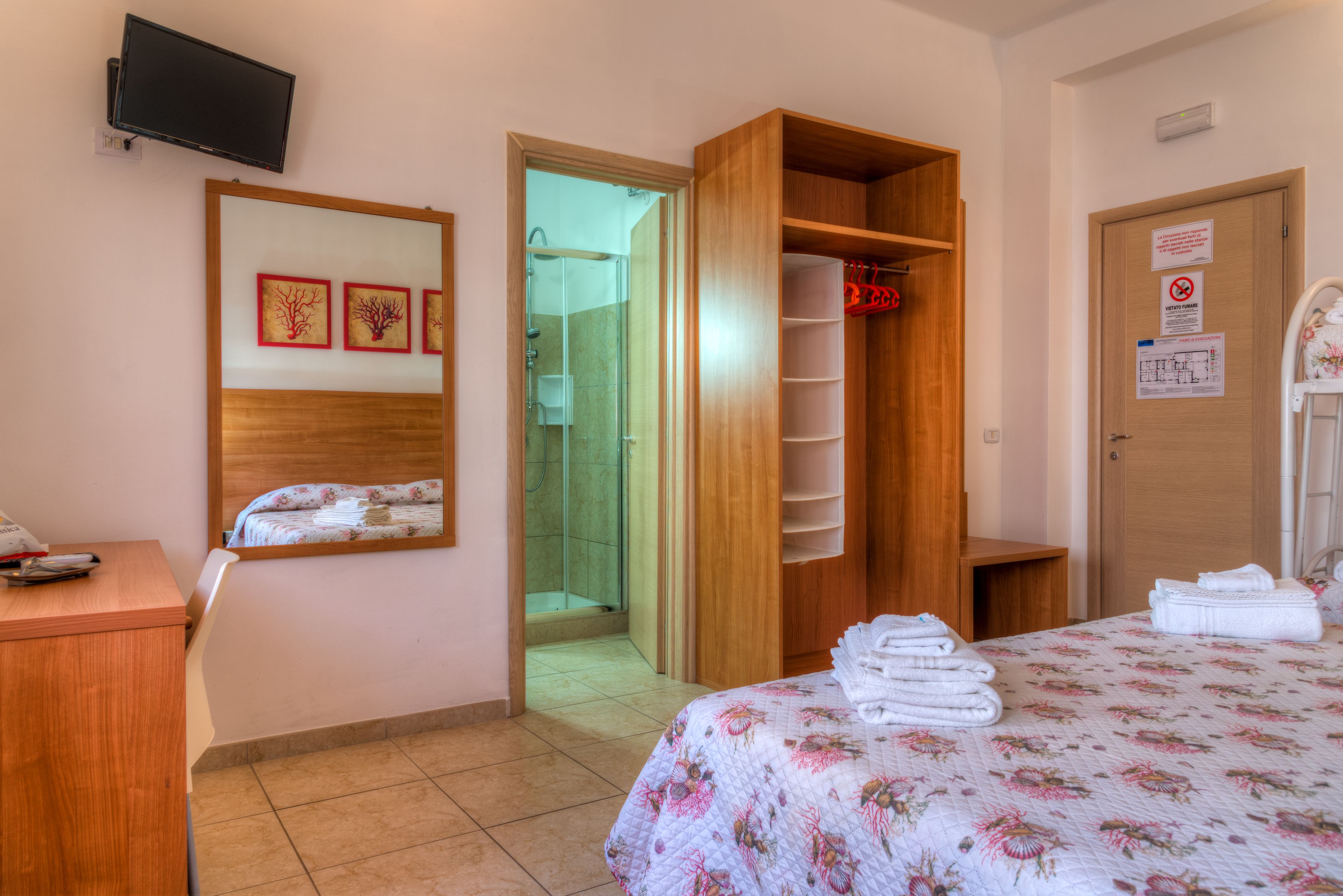 Een hotelkamer met een bed, een houten garderobe, een douche en een aan de muur bevestigde televisie.