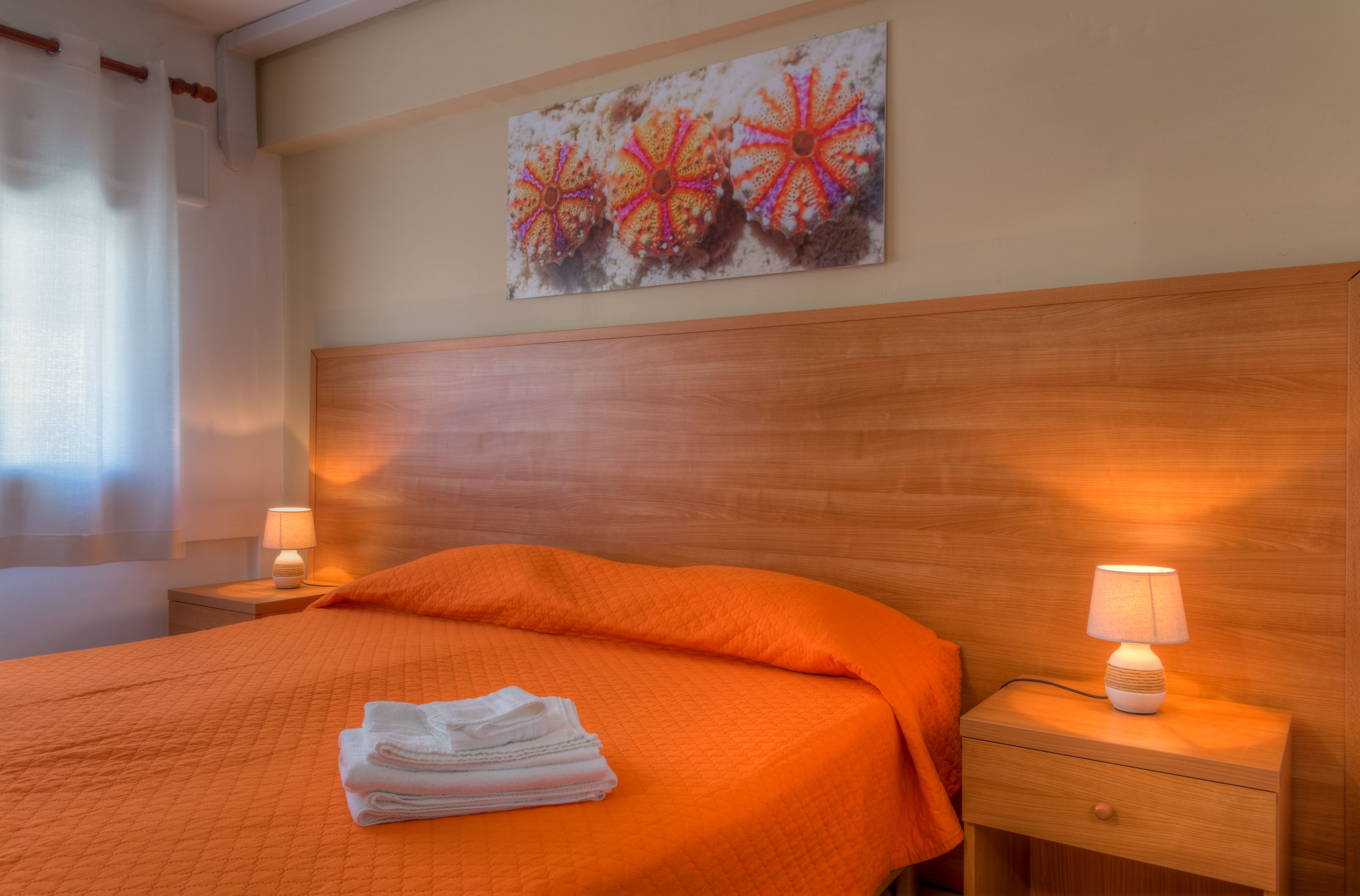 Une chambre d’hôtel avec un lit, une table de chevet avec une lampe, une serviette pliée posée sur le lit et une œuvre d’art accrochée au mur.