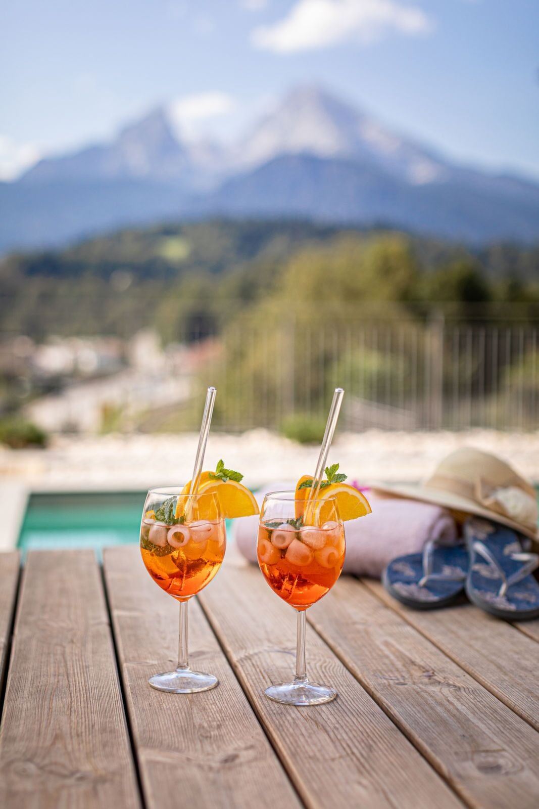 Dos vasos de una bebida con hielo y adornos sobre una mesa de madera, con vistas a la montaña al fondo.