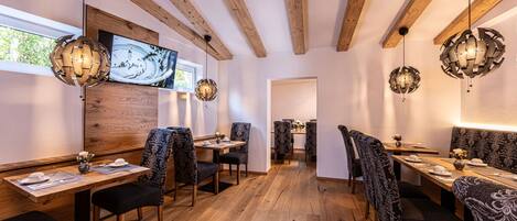 Un restaurante con vigas de madera, sillas estampadas y un televisor en la pared.
