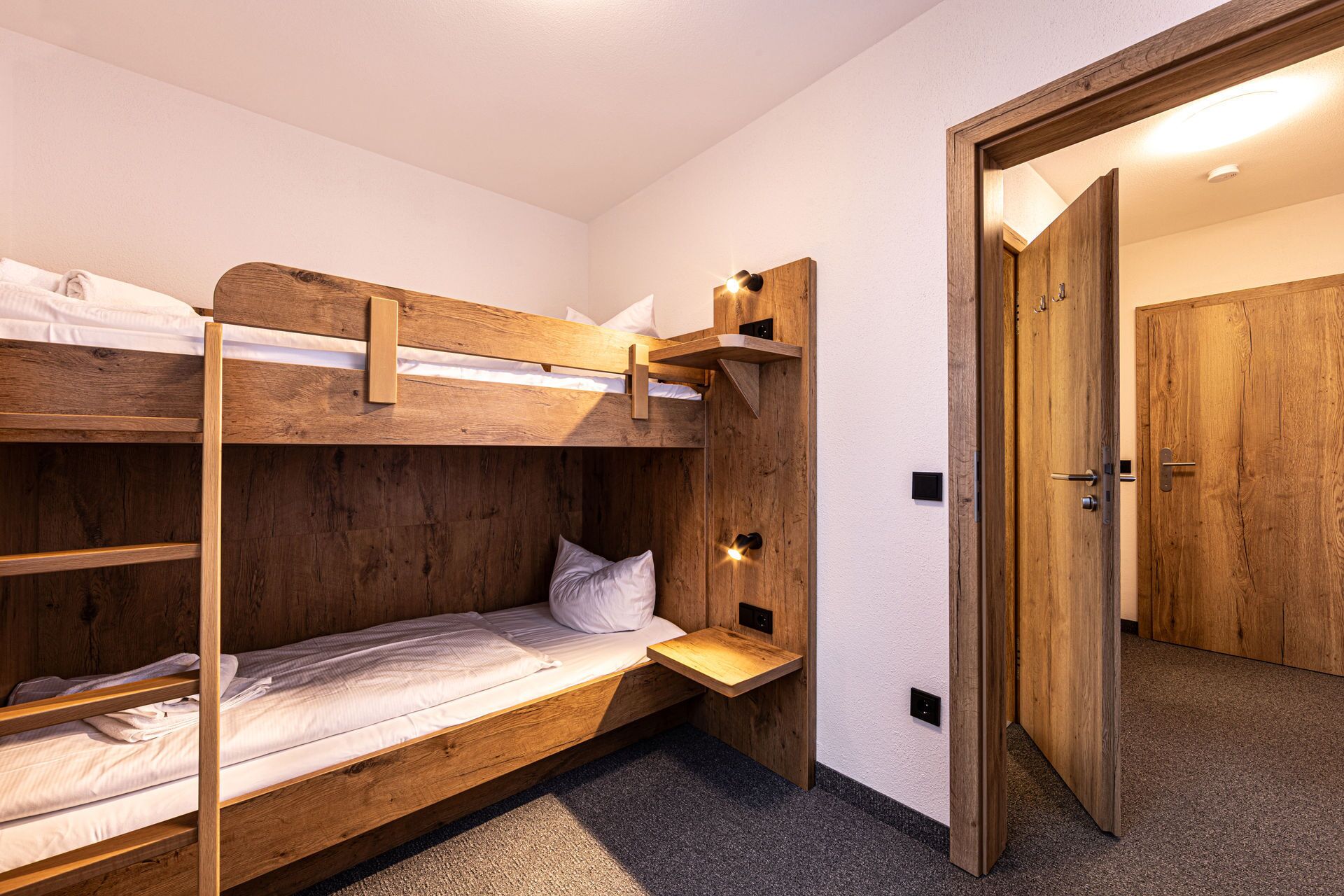 A bunk bed room with a wooden headboard, a bedside table, and a door leading to another room.