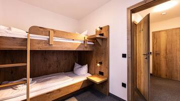 A bunk bed room with a wooden headboard, a bedside table, and a door leading to another room.