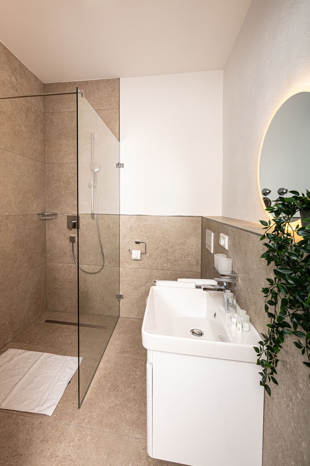 Une salle de bain moderne avec une douche à parois de verre, un lavabo blanc et un miroir doté d’un éclairage circulaire.
