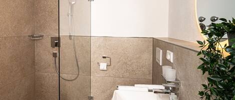 A modern bathroom with a glass-enclosed shower, a white sink, and a mirror with a circular light.