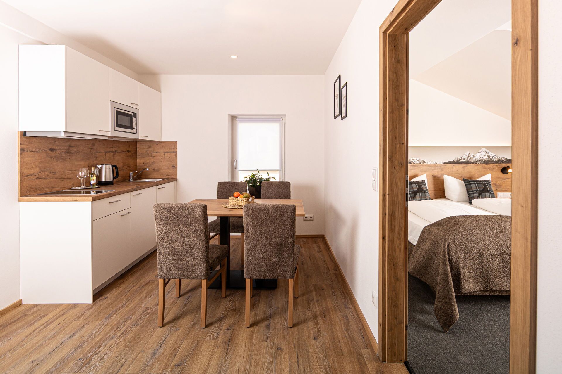 Ein kompaktes Hotelzimmer mit Küchenzeile, einem Essbereich mit Tisch und Stühlen sowie einem Bett mit Blick auf die Berge.