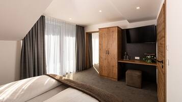 A modern bedroom with a bed, a wooden wardrobe, a TV, and a small seating area.