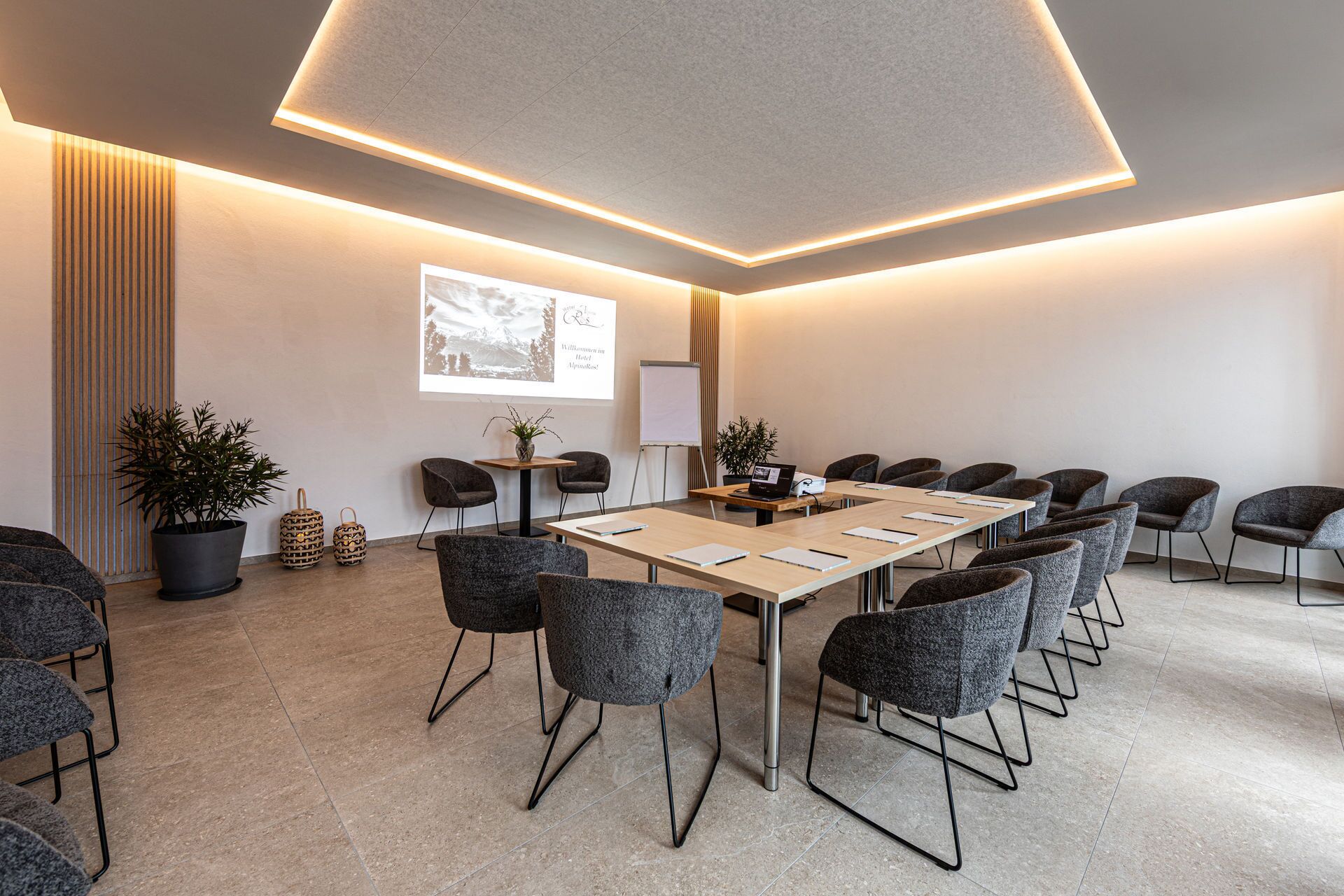 Ein moderner Konferenzraum mit einem langen Tisch, mehreren Stühlen, einem Projektor und einer Whiteboard-Wand.