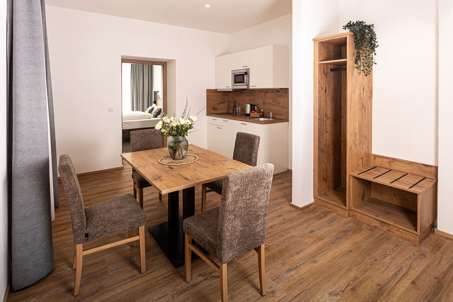 A modern kitchen with white cabinets, a microwave, and a wooden bench with a plant.